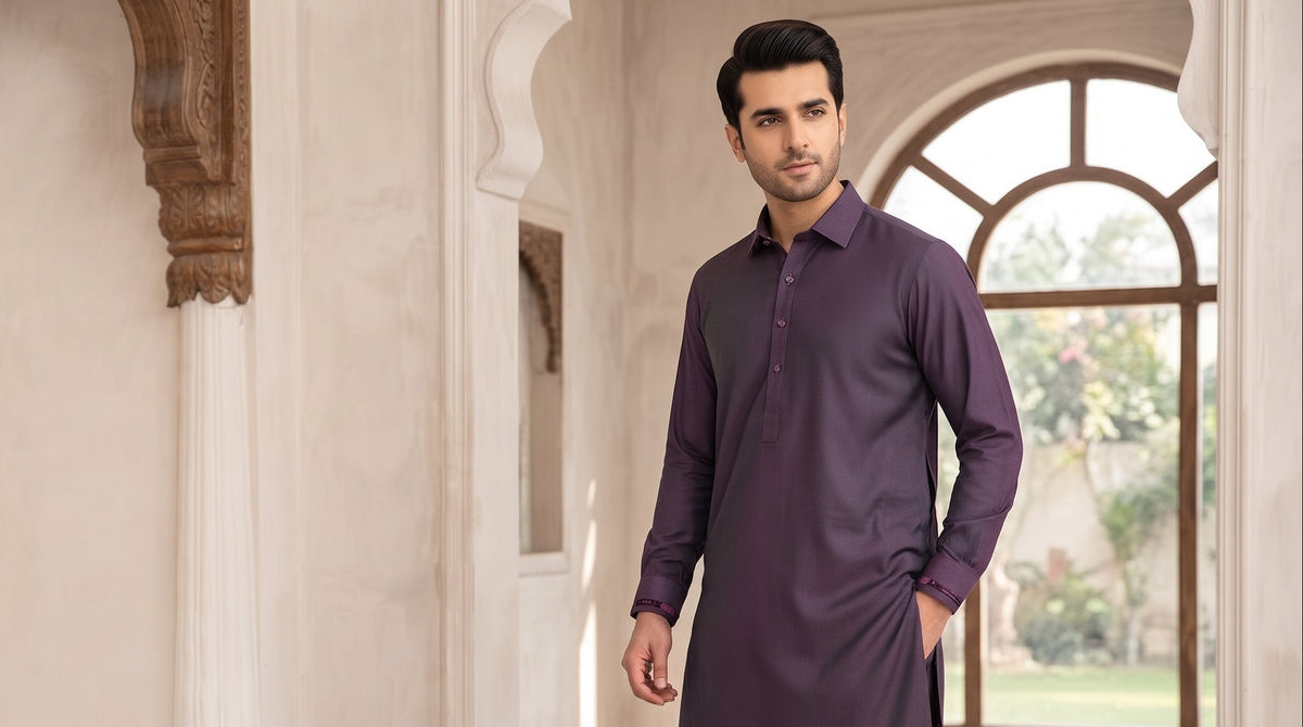 A man wearing a double-tone purple kurta and matching trousers stands in a traditional architectural corridor with carved pillars and arched windows.